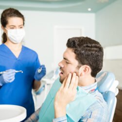 Mid adult man suffering from toothache while looking at dentist with tools in clinic